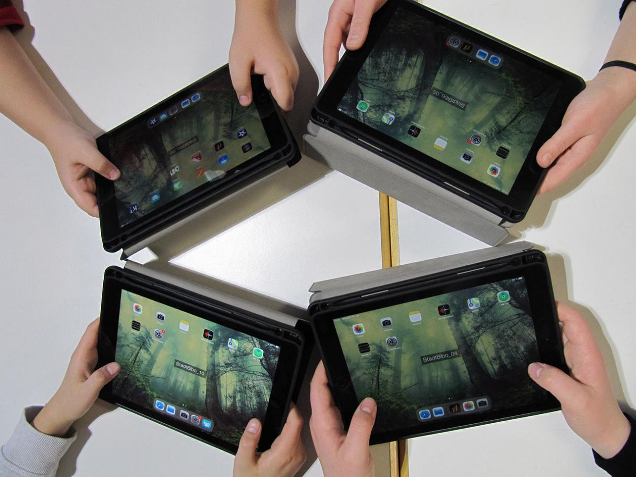 Four tablets held in a circle by four pairs of hands
