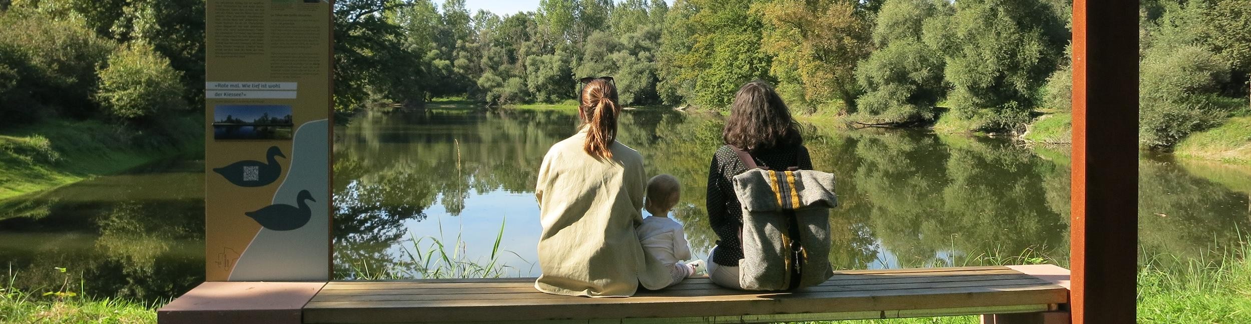 Two women and a child sitting at a station of the Rheinauen-Runde