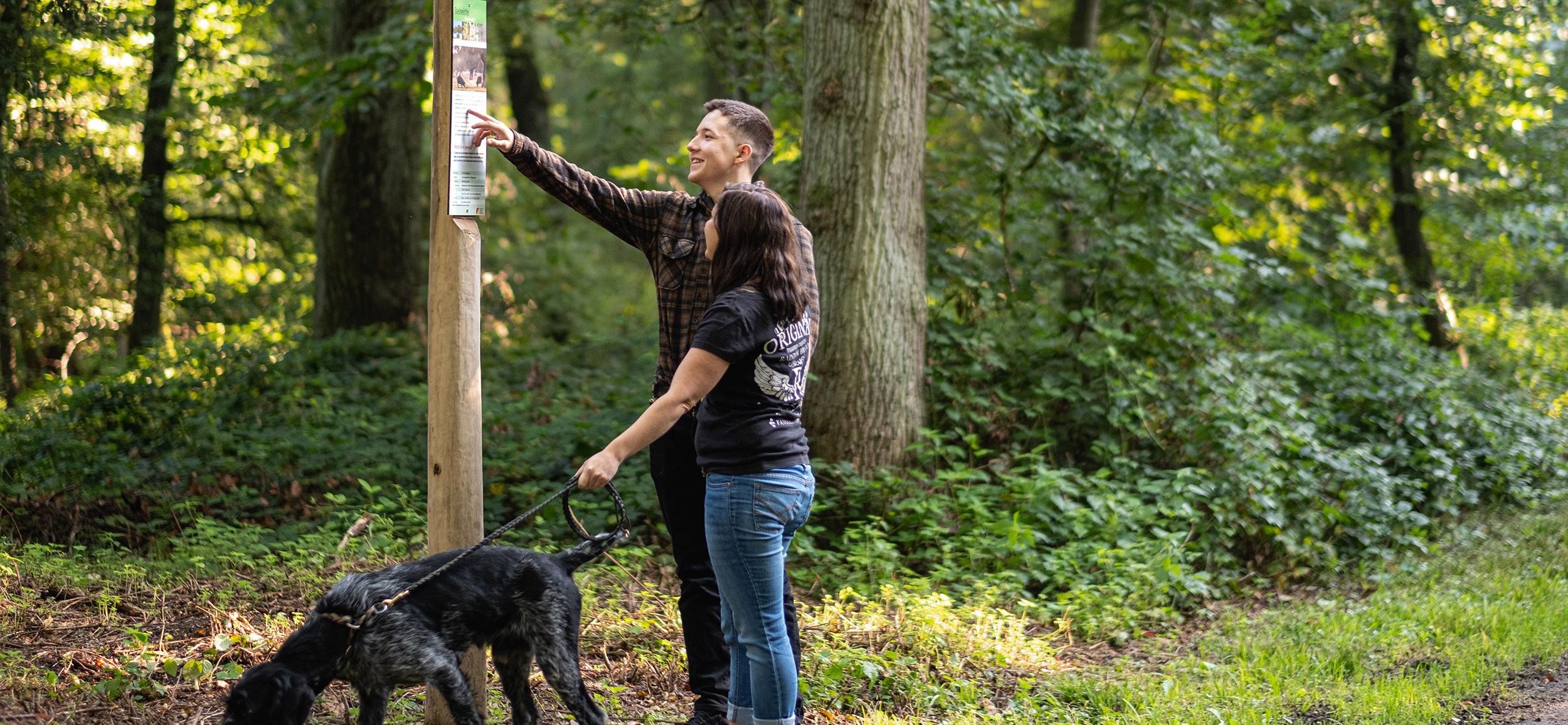 Frau, Mann und Hund stehen an einer Infotafel im Stadtwald Rastatt