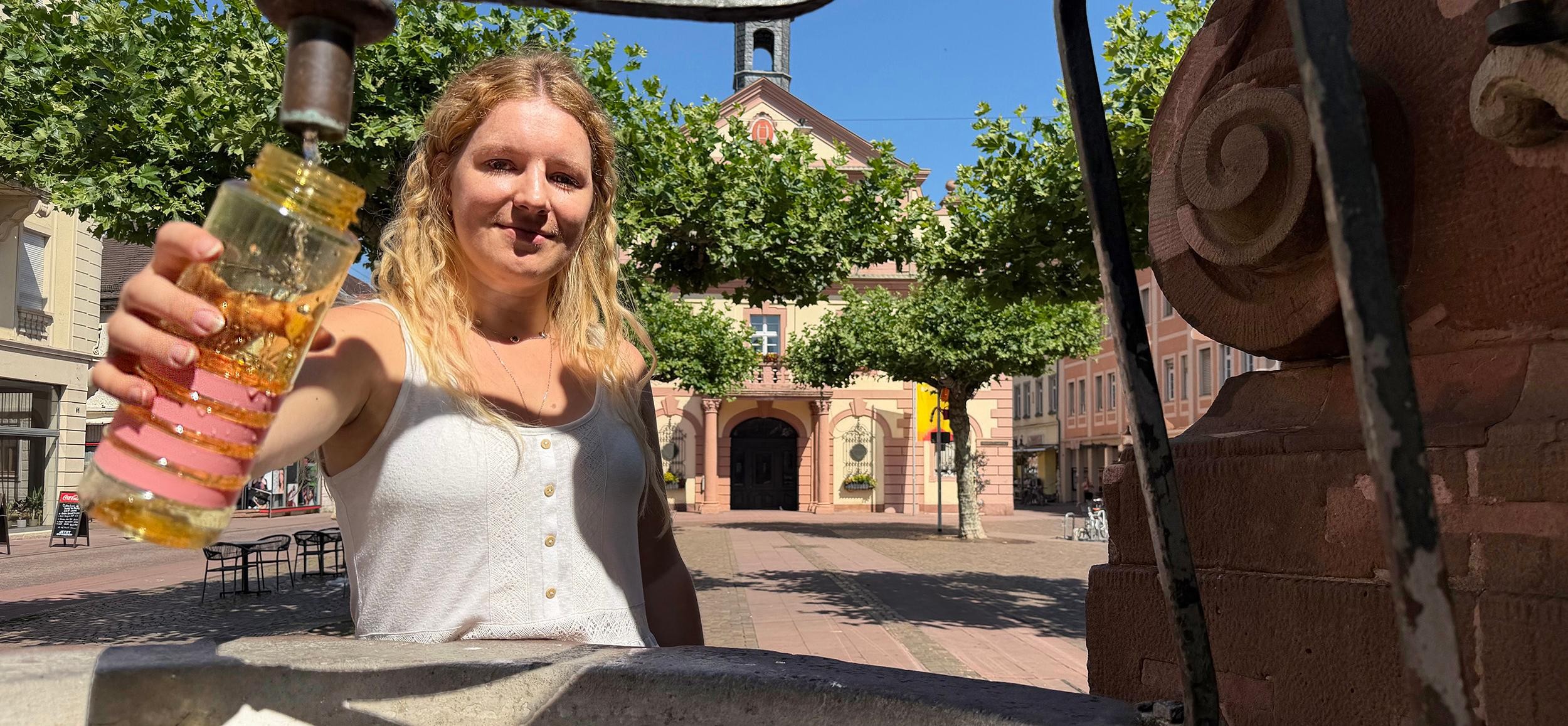 Frau steht am Alexiusbrunnen und füllt Trinkflasche auf
