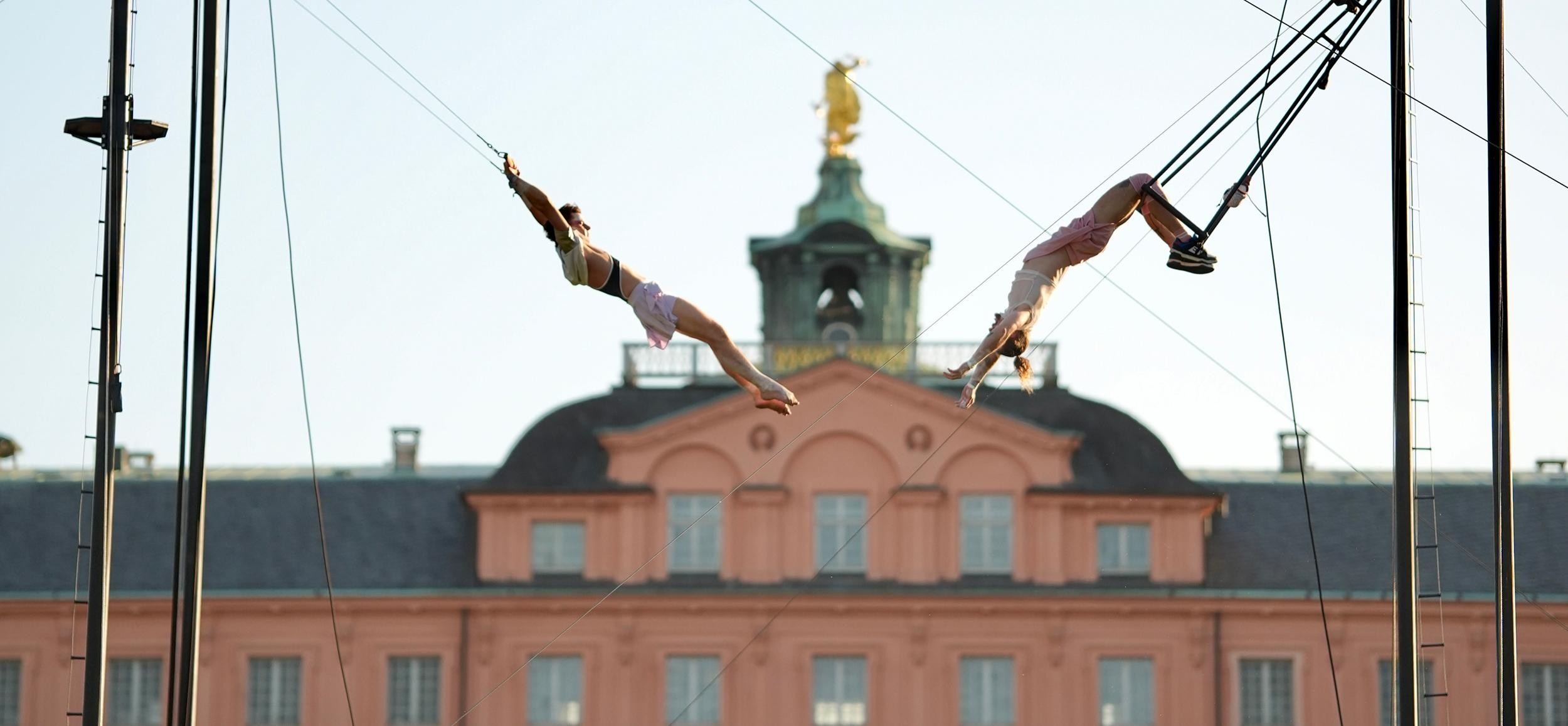 Zwei Künstler schwingen auf einem Trapez vor der Schlosskulisse