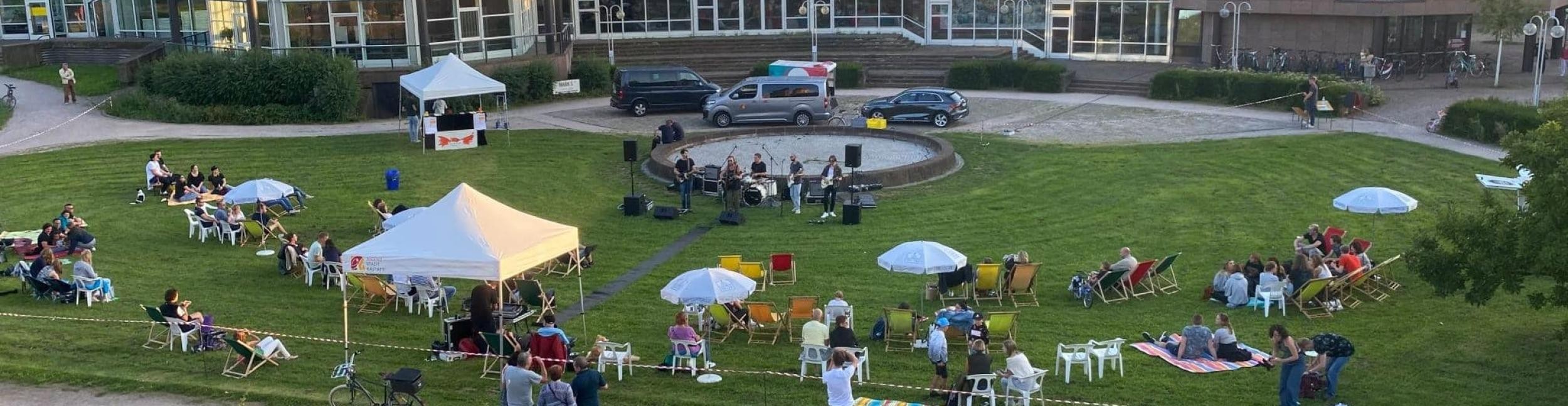 Murgchillout Rastatt - Auf einer Wiese sitzen viele Menschen auf Liegestühlen, davor spielt eine Band Musik, im Hintergrund Gebäude