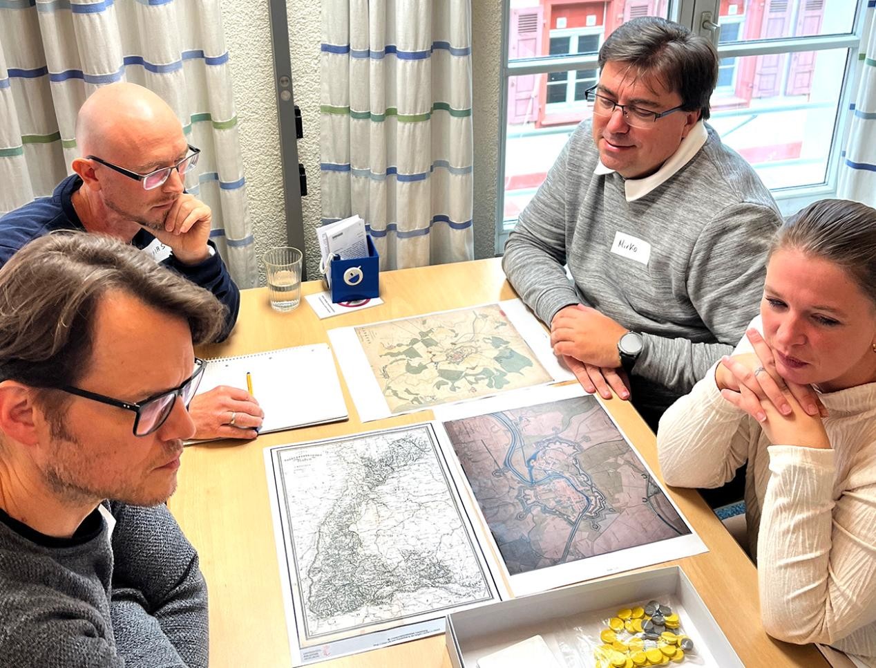Ob Spielstein oder Karten. Für ein Brettspiel sind keine Grenzen gesetzt. Foto: Stadt Rastatt/Birgitt Stellmach Teilenhmerinnen und Teilnehmer sitzen am Tisch und erfinden Brettspiel