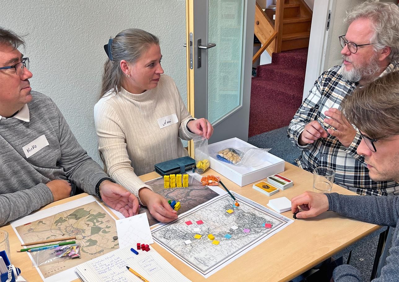 Die Teilnehmerinnen und Teilnehmer haben viel Freude beim Erfinden der Spiele. Foto: Stadt Rastatt/Birgitt Stellmach Teilenhmerinnen und Teilnehmer sitzen am Tisch und erfinden Brettspiel