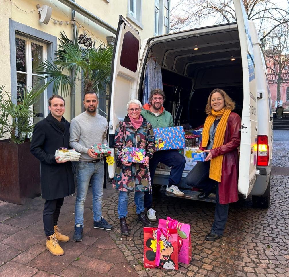 Ein Lieferwagen voll Weihnachtsfreude: 250 Geschenke für Kinder sind bei der diesjährigen Aktion Wunschbaum zusammengekommen. Viele fleißige Hände helfen beim Einladen (v.r.: OB Monika Müller, Sven Reutner, Corinna Kopf, Ehsan Niesi, Christian Römmich). Foto: Isabelle Joyon / Stadt Rastatt. Menschen vor Lieferwagen
