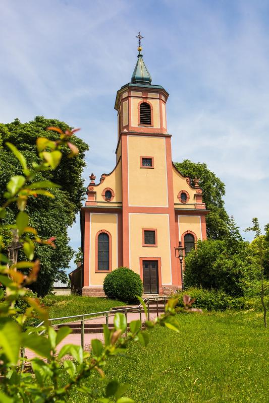 Bernhardkuskirche, blauer Himmel und üppige grüne Bepflanzung