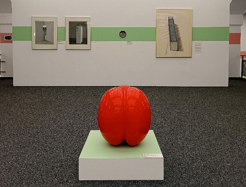 Im Vordergrund ist eine rote Plastik zu sehen, im Hintergrund verschiedene Bilder