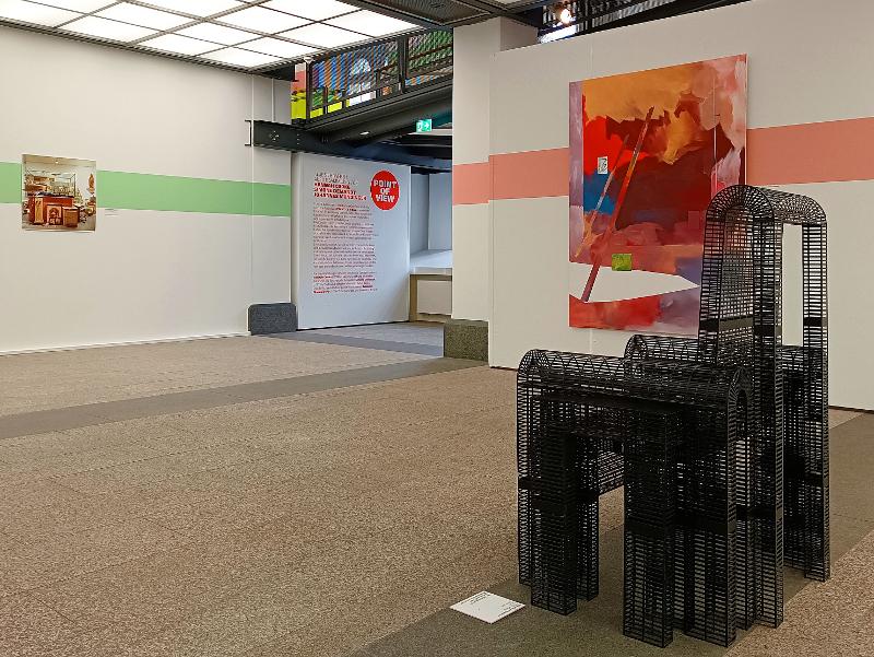 Im Vordergrund ein Stuhl aus Drahtgeflecht, im Hintergrund sind verschiedene Bilder an den Wänden zu sehen