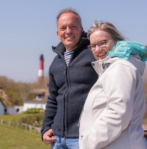 Vor dem Hintergrund des Pellwormer Leuchtturms lächeln die Autoren Markus Stephan und Katja Lund rechts im Vordergrund dem Bildbetrachter freundlich entgegen