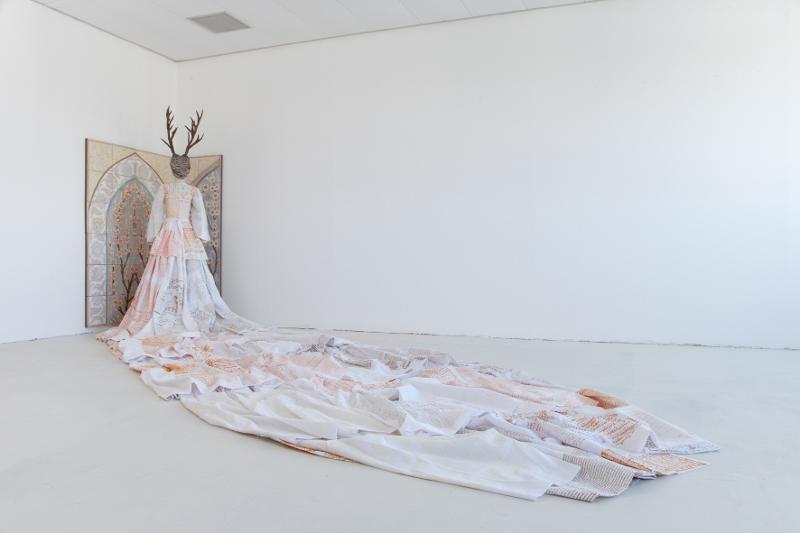 Mona Hakimi-Schüler: Multi-bodies - Installation I, going to the lucky house in white dress, leaving it with white shroud. Foto: Michael Klaus Figur, welche mit dem Rücken zum Betrachter in einer Ecke steht in einem Kleid mit sehr langer Schleppe, an der Wand sind über Eck Bildtafeln angebracht
