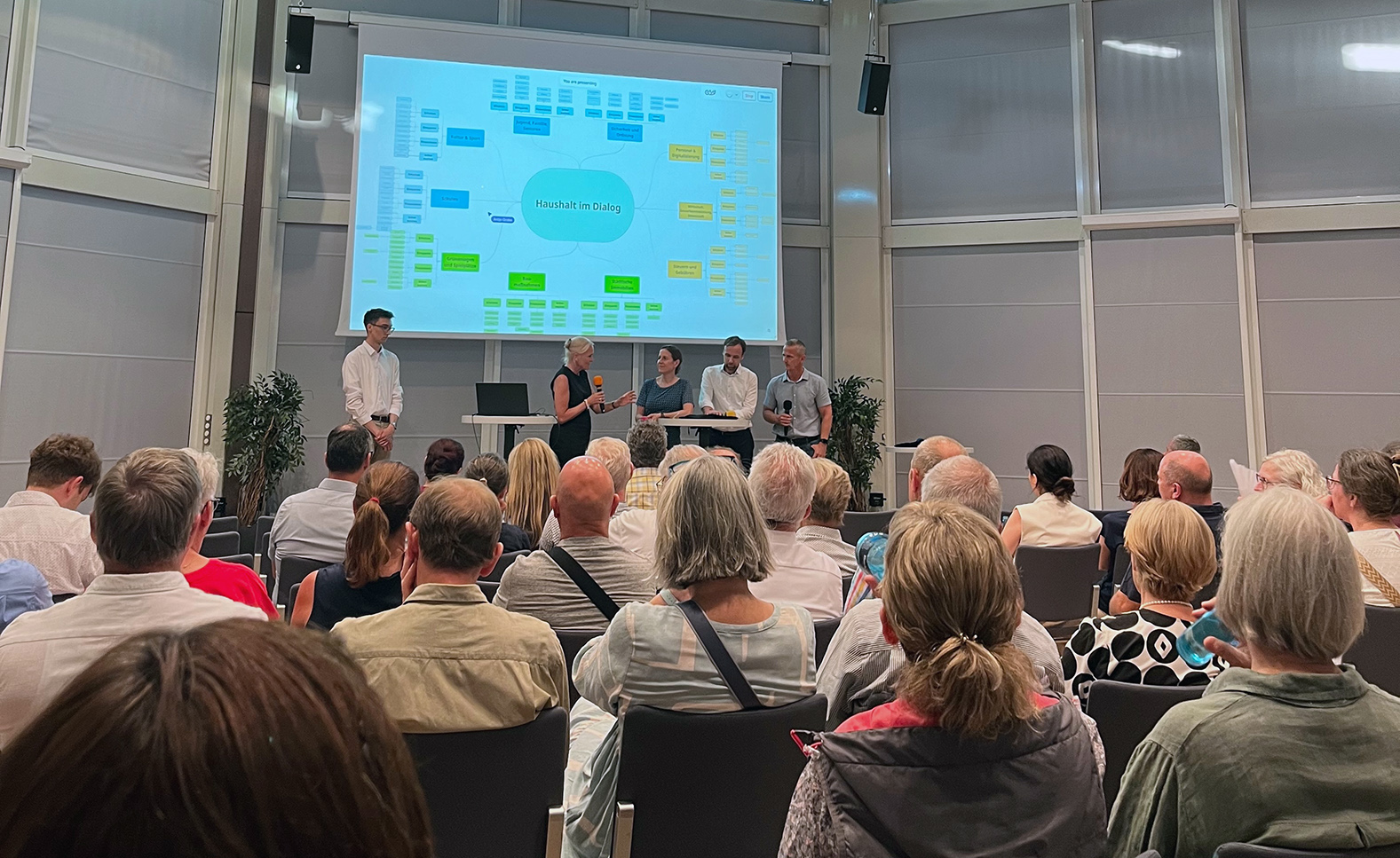Menschen sitzen in der BadnerHalle bei der Infoveranstaltung Haushalt im Dialog