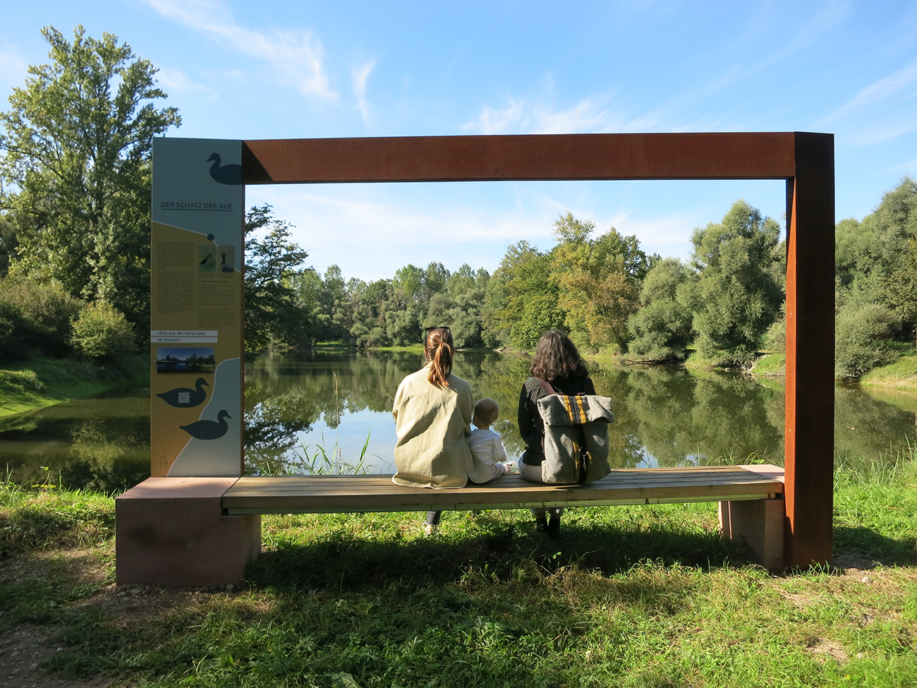 Zwei Frauen und ein Kind sitzen in dern Rheinauen auf einr Bank