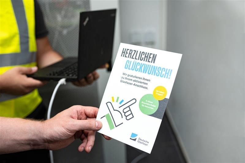 Symbolfoto Hausanschluss Deutsche Glasfaser Mann hält Flyer zur Glasfaser in der Hand