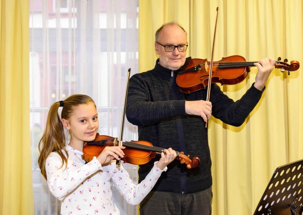 Junges Mädchen und Musiklehrer spielen gemeinsam Geige